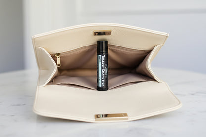 Beige clutch bag with a black tube of chap stick inside on a light gray background