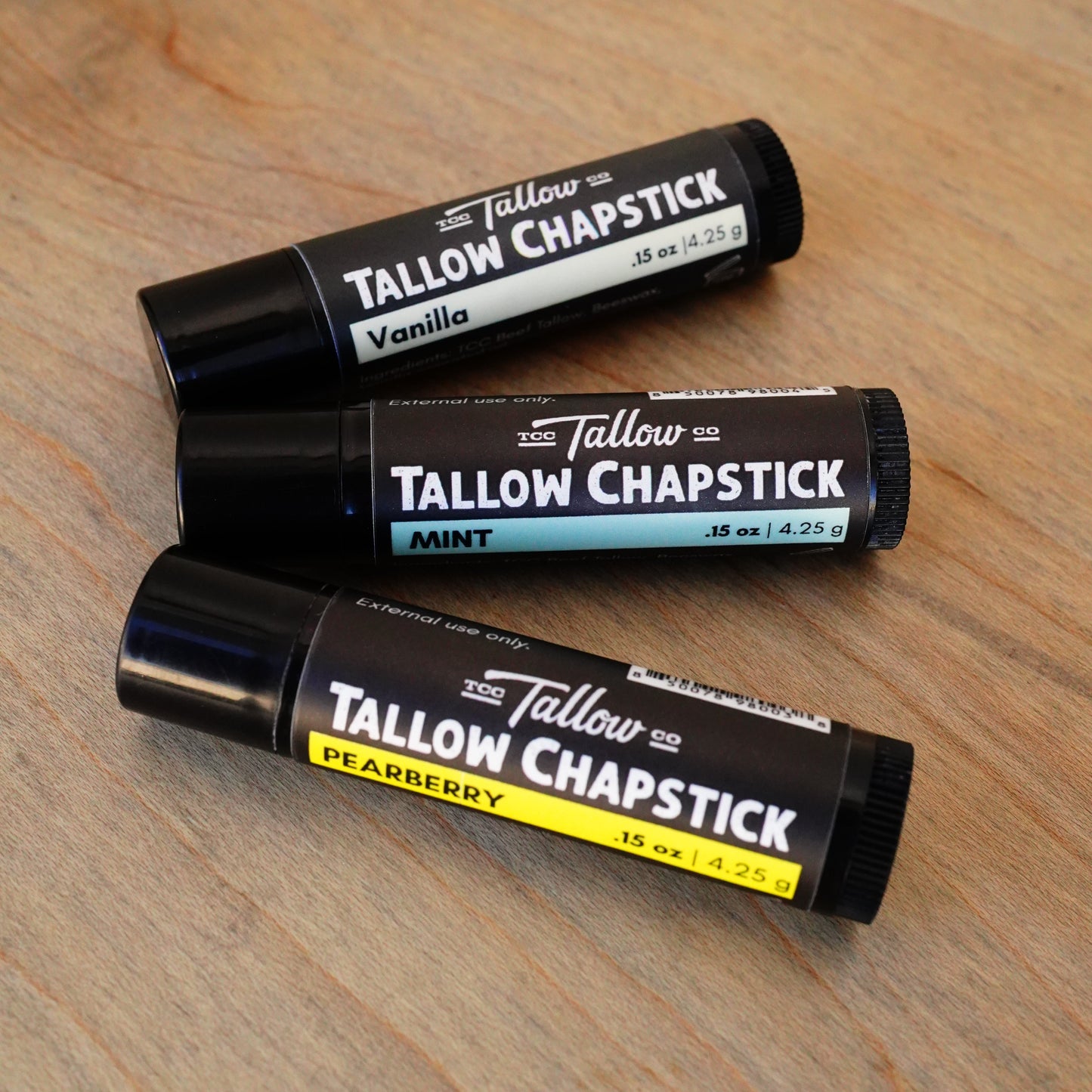 Three Tallow Chapstick tubes on a wooden surface