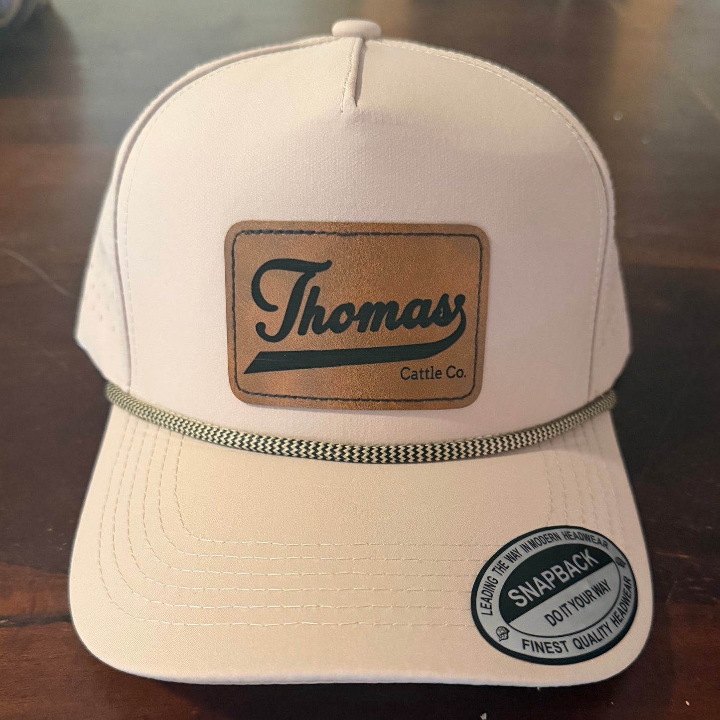 Beige cap with 'Thomas' logo on a reflective surface