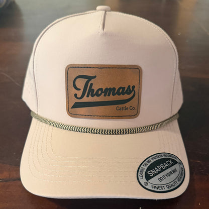 Beige cap with 'Thomas' logo on a reflective surface