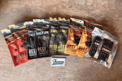 Assorted packages of beef jerky on a wooden surface with a Thomas brand label.