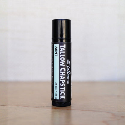 Tallow Chapstick container on a wooden surface with a white background