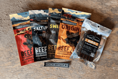 Assorted packages of Thomas Cattle beef jerky on a wooden surface