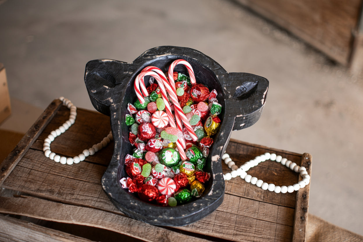 Decorative black mitten filled with colorful candies on a wooden surface.